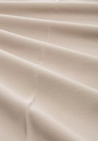 Beige textured fabric with visible folds and a smooth surface, featuring a soft sheen. Material appears stretchy and lightweight.
