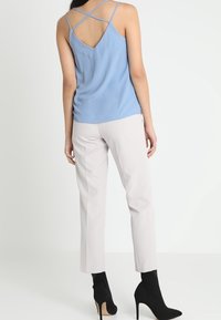 Ljusblå silkeslinne med korslagda ryggremmar, parat med ljusbeige skräddarsydda byxor och svarta klackade ankelstövlar.