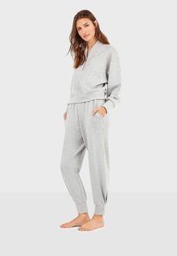Grijze loungewear set van twee delen, gemaakt van zacht materiaal, met een sweatshirt met halve rits en een voorkantzak en broek met elastische boorden en zakken.