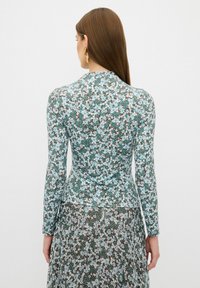 Langärmliges Blumenkleid in Türkis, Braun und Weiß. Es hat ein tailliertes Oberteil, einen weit ausgestellten Rock und einen strukturierten Stoff mit kleinen Blumenmustern.
