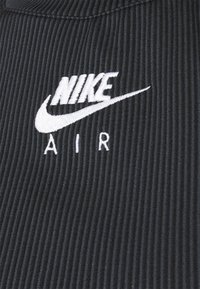 Tessuto nero a coste con ricami bianchi dei loghi "NIKE" e "AIR". Il design include linee distintive per aggiungere texture.
