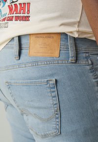 Heled taev Blue denim püksid nahkplaasiga, millel on taga vööl silt "JACK & JONES", eristuva õmblusega ja klassikalise tasku kujuga.