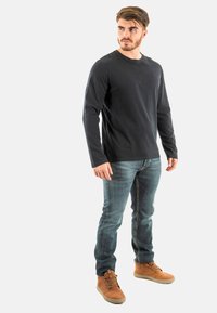 Czarny długi rękaw t-shirt, dopasowany krój, w połączeniu z niebieskimi dżinsami. Brązowe buty za kostkę z sznurowadłami, widoczną teksturą i swobodnym krojem.