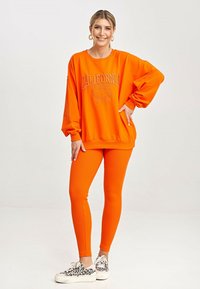 Pomarańczowa bluza z nadrukiem "CALIFORNIA", w zestawie z pomarańczowymi, prążkowanymi legginsami. Białe sneakersy w czarny wzór leopardzi.