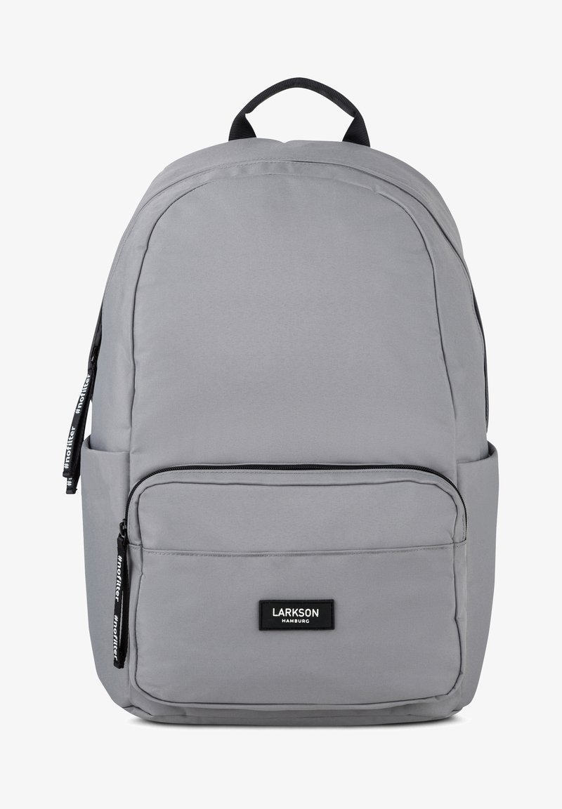 Szürke anyagú hátizsák lekerekített formával, elülső cipzáras zsebbe, oldalsó vízpalack zsebbe és felső fogantyúval. Fekete márka címkével rendelkezik.