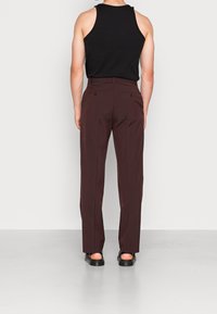 Bordeauxrode broek met een rechte snit, gladde stoftextuur, twee achterzakken met knopen, gecombineerd met een mouwloos zwart tanktop.