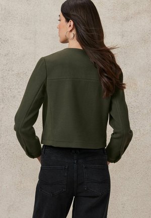 Dark green cropped jacket in soft fabric, featuring long sleeves and a clean neckline. Paired with dark denim jeans with subtle stitching.