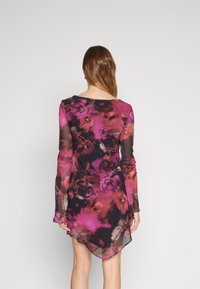Robe à manches longues en tissu transparent, ornée d'un motif floral dans des tons de rose et de noir, avec un ourlet asymétrique et une texture délicate.