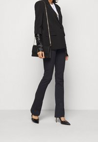 Blazer nero oversize con spalle strutturate, abbinato a pantaloni neri a zampa. Gli accessori includono una piccola borsa nera e tacchi a punta.