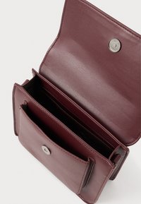 Ciemnoczerwona skórzana portmonetka otwarta, ukazująca liczne przegródki oraz przednią kieszeń z metalowym zapięciem magnetycznym w kolorze srebrnym.