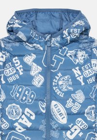 Blau gepolsterte Jacke mit Kapuze, weißen, sportlichen Grafiken wie Tigern, Fußbällen und Texten wie "GAP 1969" und "NY EST."