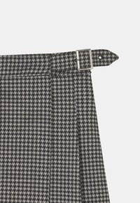 Houndstooth-mønstret nederdel i sort og grå stof. Har et bælte med en sølvspænde i taljen og pleats for tekstur.