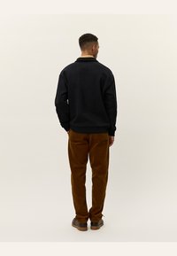 Sudadera negra con cuello, combinada con pantalones de pana marrones. El conjunto tiene un corte relajado y un sutil contraste de texturas.