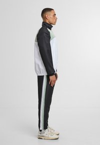 Träningsdräkt bestående av en svart jacka med vita och mintgröna paneler, i kombination med svarta byxor med vita och mintgröna ränder.