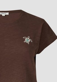 Bruine t-shirt van zachte stof met een witte omtrek van een schildpad en een meerkleuren ontwerp op de borst. Korte mouwen, ronde hals.