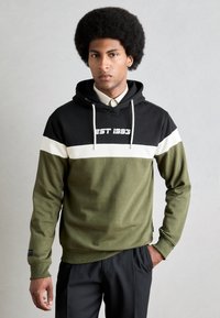 Hettegensere i svart, hvit og oliven grønn, med "EST 1993" trykket på brystet. Kofte av bomull, standard passform, ribbestrikkede mansjetter og hem.