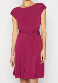 Sukienka magenta do kolan z krótkimi rękawami, okrągłym dekoltem i materiałowym paskiem w talii. Miękka, gładka tekstura z płynącą sylwetką.