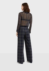 Průhledná černá kostkovaná blůza s dlouhými rukávy, kombinovaná s kalhotami s širokými nohavicemi v námořnické kostce, které mají šedé pruhy a vysoký pas.