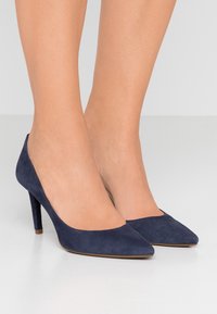 Námořnické modré semišové lodičky na vysokém podpatku s špičatou špičkou a elegantní siluetou, se hladkým povrchem a štíhlým stiletto podpatkem.