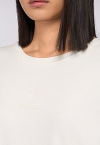 Felpa color beige chiaro con collo rotondo, caratterizzata da un logo Trussardi a rilievo discreto sul petto. Tessuto morbido con una consistenza liscia.