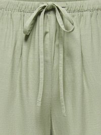 Pantalones verde claro con cinturilla elástica fruncida y cordón ajustable anudado al frente, mostrando la textura de la tela y detalles sutiles de costuras.