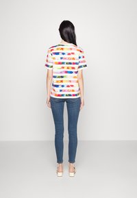 Camiseta de rayas multicolores de manga corta, hecha de una tela suave. Combinada con jeans ajustados azules y sandalias de tacón bloque de colores claros.
