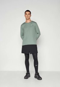 Haut Nike à manches longues vert, shorts noirs et leggings noirs. Présente le logo Nike sur le haut et les chaussures, style athlétique et coupe ajustée.