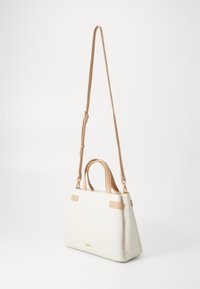 White faux leather handbag with tan accents and longer shoulder strap. Features two handles and gold hardware. Triangular shape.