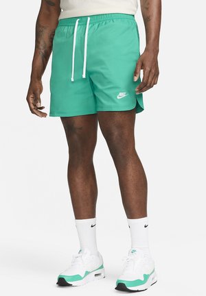 Bañador Nike turquesa con cinturilla elástica, cordones blancos y pequeño logo. Tela suave, corte por encima de la rodilla.