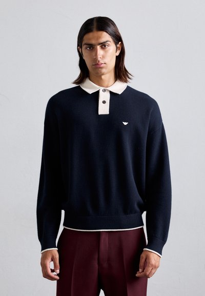 Maglione attillato blu navy con colletto crema a contrasto e due bottoni scuri. Presenta un logo sul petto e polsini e orlo a costine.