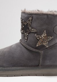 Šedá semišová kotníková bota s dvěma hvězdicovými ozdobami s krystalovými detaily. Měkké podšívání vykukuje nahoře, boty mají odolnou podrážku.