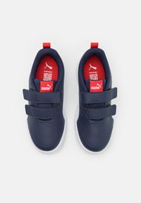 Baskets synthétiques bleues avec deux bandes velcro noires, semelle extérieure blanche et accents intérieurs rouges. Présente une étiquette de logo sur la languette.