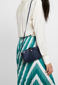 Borsa a tracolla rettangolare in stampa serpente blu navy, con superficie testurizzata e lunga tracolla. Presenta una chiusura a scatto e una ferramenta discreta.