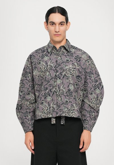 Camicia corta con colletto in tessuto grigio, decorata con motivi floreali e foglie neri e verdi. Presenta una chiusura a bottoni frontale e maniche ampie.