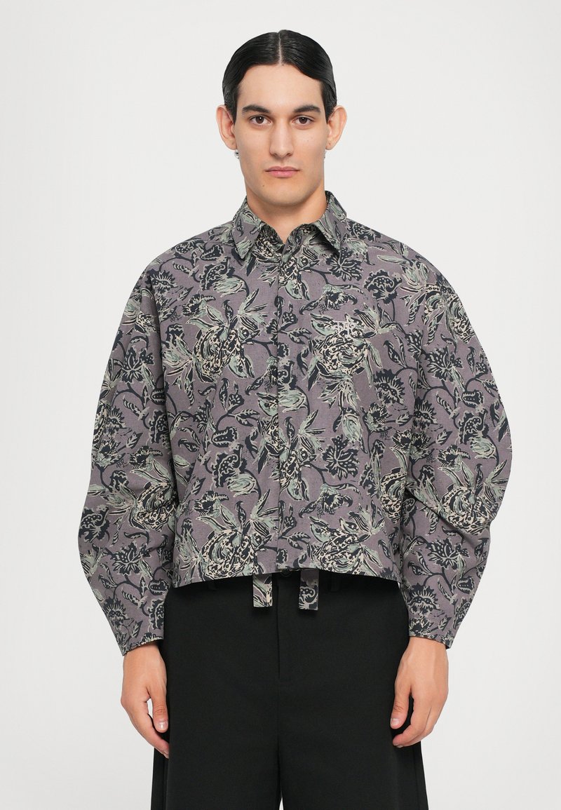 Geknöpftes, kurzes Hemd aus grauem Stoff mit floralen und blattartigen Mustern in Schwarz und Grün. Verfügt über eine Knopfreihe vorne und lockere Ärmel.