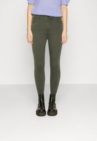 Olive green skinny jeans with a smooth texture and five-pocket design, paired with black platform ankle boots.