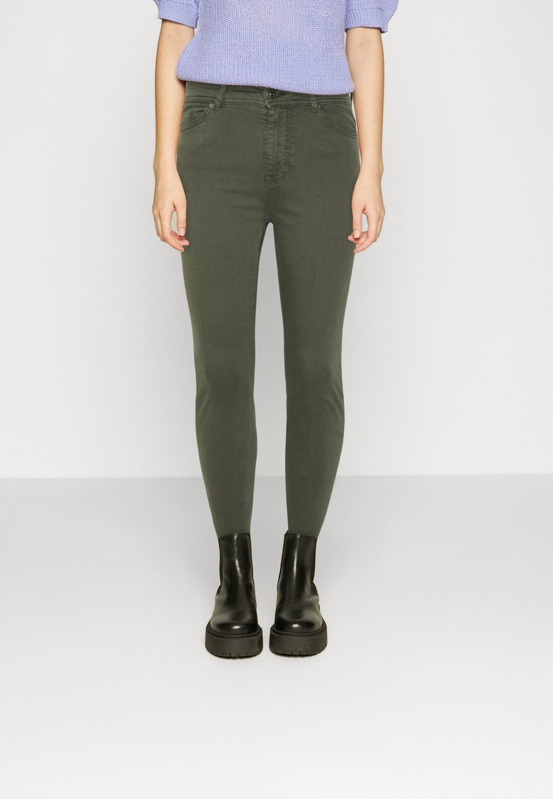 Olive green skinny jeans with a smooth texture and five-pocket design, paired with black platform ankle boots.
