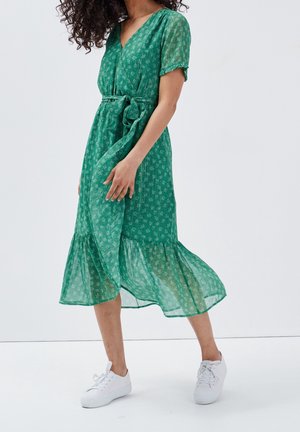 Zielona, zwiewna sukienka z dekoltem w serek, krótkimi rękawami i paskiem do wiązania. Posiada falbaniany dół i kwiatowy wzór na lekkiej tkaninie. Noszona z białymi trampkami.