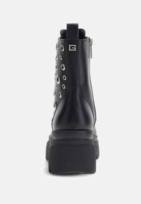 Stivaletto alla caviglia in pelle nera con punta arrotondata, suola spessa a piattaforma e dettagli argentati con occhielli lungo il lato; cerniera metallica sul retro.