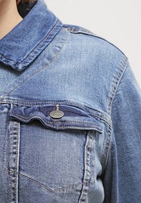Jeansjacka i ljusblå färg med en vikkrage och en bröstficka med knappdetalj. Tyget har en klassisk urtvättad struktur.