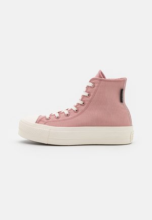 Baskets montantes en velours côtelé rose avec lacets blancs et semelle en caoutchouc blanche épaisse sur fond uni.