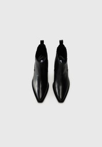 Botas de cuero negro hasta el tobillo con un diseño de punta afilada, textura suave y lengüetas para ponerlas fácilmente, con sutiles detalles de puntadas.