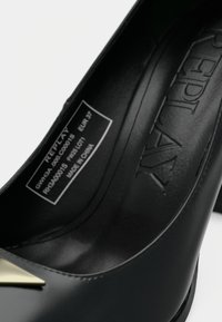 Scarpa nera in pelle con tacco alto e un accento metallico a punta. Presenta una texture liscia e un logo impressionato sulla soletta. Misura EUR 37.