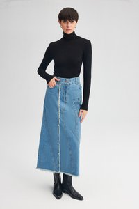 Dolga jeanskrila s strgani robom, sprednjimi žepi in gumbastim pasom. Nošena čez črno turtlenecko in v kombinaciji s gležnjarji.