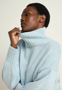 Light blue turtleneck sweater in soft, textured knit with ribbed accents on collar and cuffs, showcasing a relaxed fit and oversized silhouette.