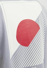 Gaiši pelēks T-krekls ar baltu grafiku, kurā ir liels sarkans aplis, diagonālas līnijas un smalki teksturēti akcenti. Ikdienišķs dizaina elements.