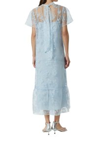 Przezroczysta, jasnoniebieska sukienka w kwiaty z wiązaniem przy dekolcie, krótkimi rękawami i falbanistym dołem. Charakteryzuje się zwiewnym krojem i delikatną fakturą.