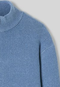 Pull en tricot côtelé bleu avec un col montant, présentant un tissu texturé et une coupe décontractée. Le design met en avant une apparence douce et confortable.