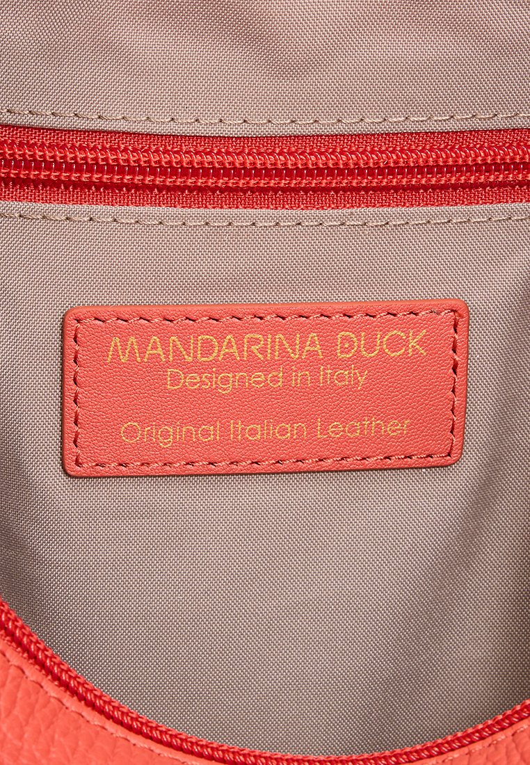 Etichetta in pelle rossa all'interno di una borsa beige con cerniera rossa, impressa con la scritta "MANDARINA DUCK Designed in Italy Original Italian Leather" in lettere gialle.