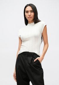 Λευκό ριγωτό τοπ με κοντά μανίκια και ψηλό λ�αιμό, σε συνδυασμό με φαρδιά μαύρα παντελόνια. Το ύφασμα έχει λεία υφή και εφαρμοστή σχεδίαση.